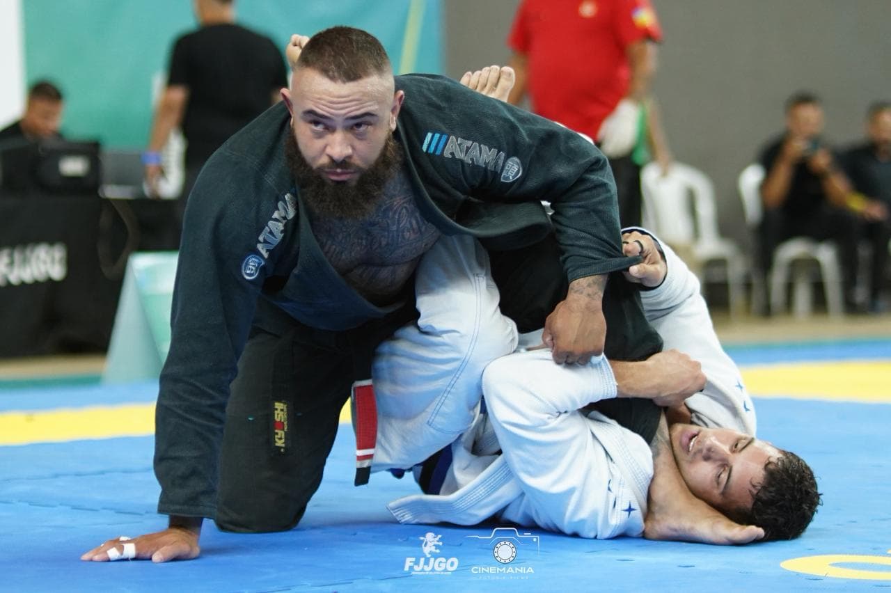 Uriel Meneses de kimono preto passando a guarda do adversário em uma competição da FJJGO