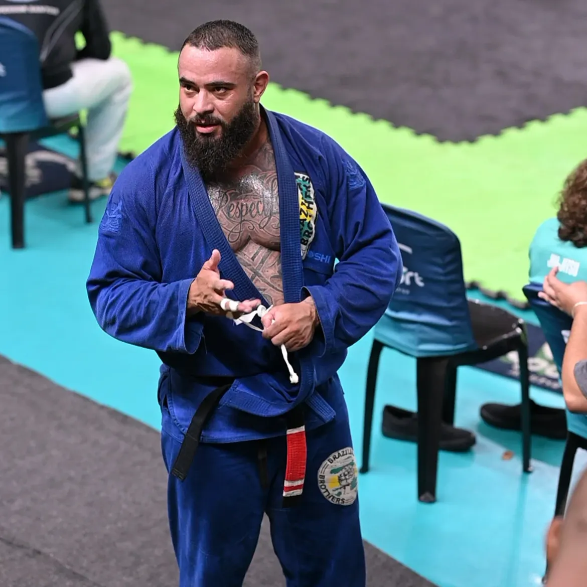 Uriel Meneses ajustando a faixa preta durante uma competição de jiu-jitsu com kimono azul